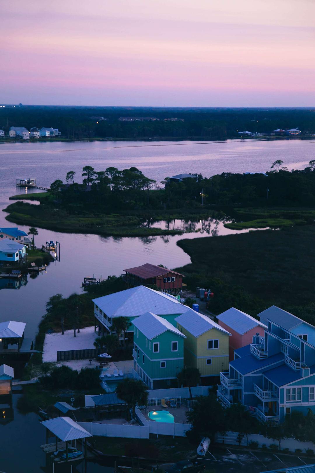 Birds eye view, violet-hued photograph of brightly colored buildings by a forested river