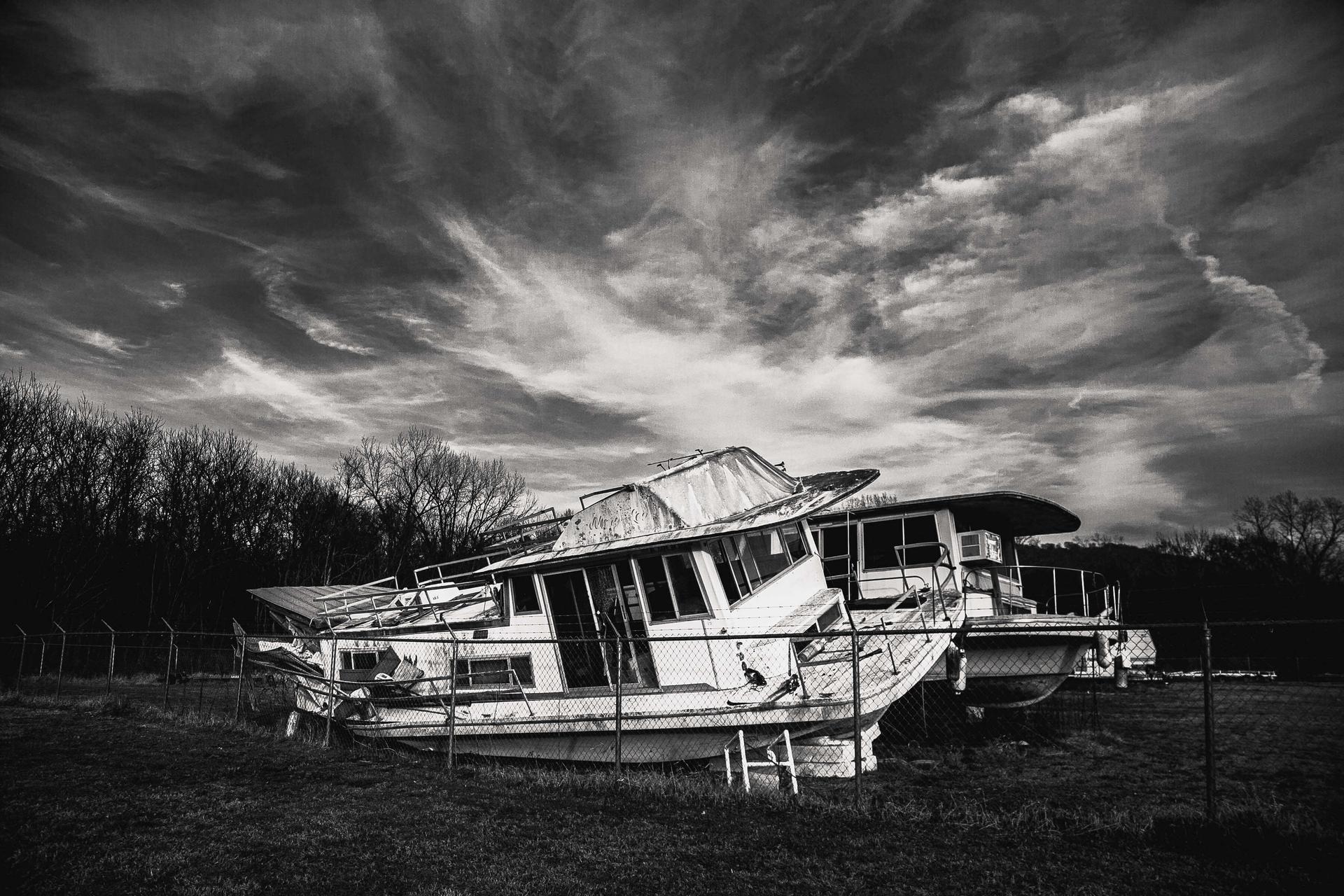 Dilapidated boat by a chain link fence.