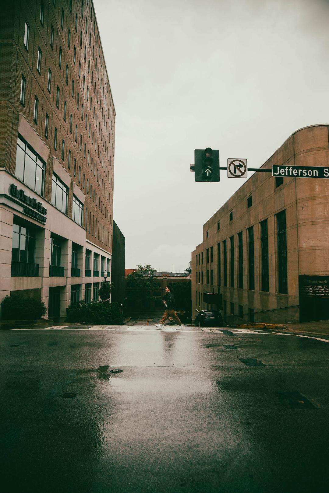 Color photo of man walking in downtown Huntsville, AL across wet pavement crosswalk